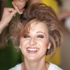 Lachende Frau, der die Haare toupiert werden für einen voluminösen Look.