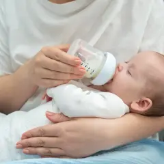 Une main tient un biberon pour nourrir un bébé endormi. La question de savoir si peut on donner de l'eau du robinet à un bébé est importante.