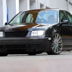 Czarny Volkswagen Bora z chromowanymi felgami stoi na ulicy.