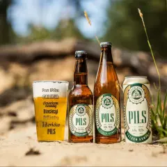 Szklanka i butelki z polskimi piwami typu lager "Pils" od Trzech Kumpli na piasku.
