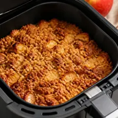 Goldbrauner Apfel Crumble aus dem Airfryer, duftend und lecker. Daneben liegen zwei rote Äpfel.