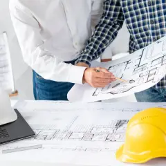 Architekci analizują plany, omawiając podział wspólnoty mieszkaniowej. Na stole leżą kaski i laptop.