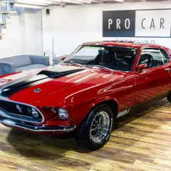 Błyszczący czerwony Ford Mustang Mach 1 z 1969 roku z czarnymi pasami na masce, gotowy do jazdy.