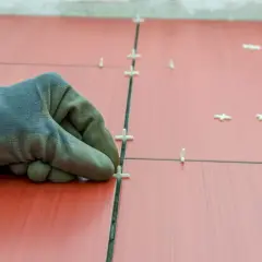 Main tenant, ganté, ajuste des croisillons pour refaire le joint du carrelage rouge.