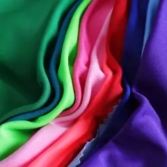 A vibrant collection of athletic wear fabric swatches in green, teal, lime, pink, red, blue, and purple, draped and folded.