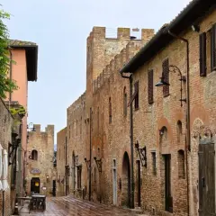 Vicoli medievali di Certaldo cosa vedere: un'antica strada in mattoni con torri merlate, lampioni in ferro battuto e finestre con persiane.