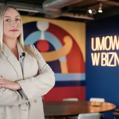 Kobieta w beżowej marynarce z mikrofonem, na tle neonu "UMOWY W BIZNESIE". Czy vider jest bezpieczny?