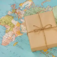 Paczka owinięta w papier i przewiązana sznurkiem leży na mapie świata. Idealna, by pokazać, co można wysłać w paczce za granicę.