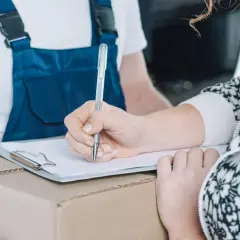Kobieta podpisuje formularz zwrotu wzór na kartonie. Kurier w niebieskim kombinezonie czeka.