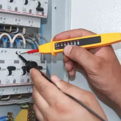 Elektryk sprawdza napięcie w skrzynce bezpieczników. Miernik wskazuje moc pozorną, pomagając zapewnić bezpieczeństwo instalacji.