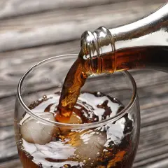 Nalewanie ciemnego napoju z butelki do szklanki z lodem. Zastanawiasz się, ile kalorii ma whisky z colą zero?