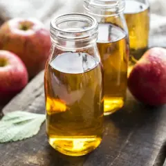 Frische Äpfel umgeben zwei Flaschen mit goldenem Apfelessig. Ein gesundes Elixier, das aus Früchten gewonnen wird.