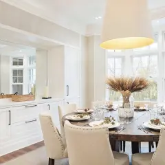 Elegant dining room inspiration featuring a rustic wooden table set for a meal, surrounded by upholstered chairs. Large windows offer a view of nature.