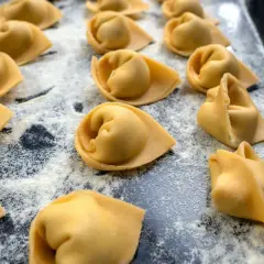 Frisch geformte Tortellini liegen auf einer bemehlten Fläche. Das Selbermachen von Tortellini ist ein Genuss für alle Sinne.