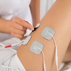Elektrostymulacja efekty uda: terapeuta umieszcza elektrody na udzie pacjentki, przygotowując do zabiegu.