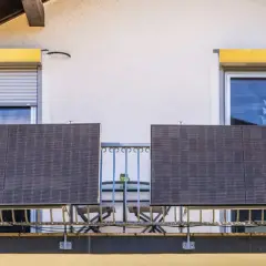 Dwa panele fotowoltaiczne na balkonie, symbolizujące odnawialne źródła energii w domu. Obok kwitnące kwiaty.