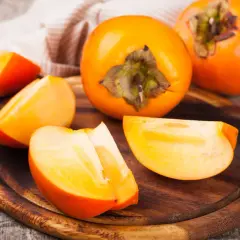 Pomarańczowe owoce kaki, pokrojone i w całości, na drewnianej desce. Odkryj owoc kaki właściwości i jego smak.