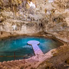 Ein atemberaubender Cenote in Mexiko mit kristallklarem, türkisfarbenem Wasser, Stalaktiten und einer steinernen Plattform.