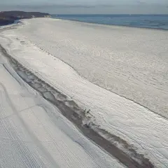 Zamarznięta Zatoka Gdańska, pokryta lodem i śniegiem, przypomina o tym, kiedy ostatnio zatoka gdańska zamarzła. W oddali widać statki.