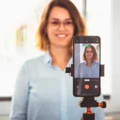 Frau macht ein bewerbungsfoto selber machen mit dem Handy auf einem Stativ.