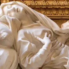 Scultura in marmo di Santa Teresa in estasi, capolavoro barocco a Roma. La sua mano sfiora il petto, mentre il volto esprime un profondo trasporto spirituale.