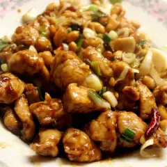 Kurczak Gong Bao z orzeszkami ziemnymi, cebulą i papryczkami chili na talerzu.