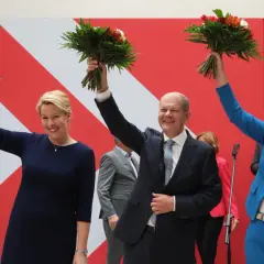 Uśmiechnięta Astrid Ann Marie Pollmann i politycy z bukietami kwiatów na tle czerwono-białej ściany.