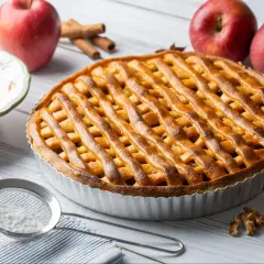 Złocista tarta z jabłkami, udekorowana kratką z ciasta, obok czerwonych jabłek i cynamonu. Idealna na jesienny deser.