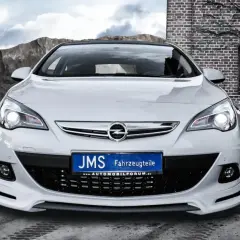 Biały Opel Astra J GTC z tuningiem JMS, z tablicą rejestracyjną "JMS Fahrzeugteile", na tle kamieniołomu i ceglanego budynku.