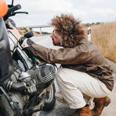 Hombre con pelo rizado revisa su moto 125, preguntándose cuanto aire lleva.