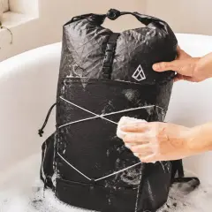 Person reinigt einen schwarzen Rucksack in einer Badewanne mit Schaum. Der Rucksack wird mit einem Schwamm abgerieben, um ihn zu waschen.