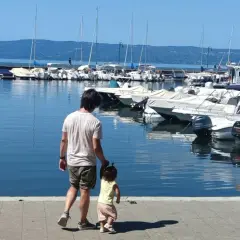 Padre e figlia passeggiano sul lungolago di Bolsena, con barche ormeggiate sullo sfondo.