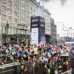 Uczestnicy biegu na 100 km startują w Poznaniu. Tłum biegaczy rusza spod wielkiego banera z napisem "START".