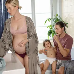 Gravid kvinna vid handfatet, medan pappan borstar barnets tänder. Vanliga flytningar gravid är normalt.