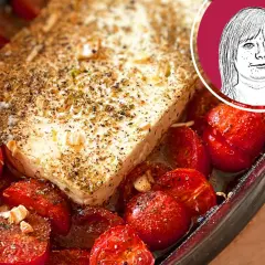 Ein Block Feta mit Kräutern und Gewürzen, umgeben von gebackenen Kirschtomaten. Perfekt für ein schnelles Gericht mit Nudeln mit Feta.