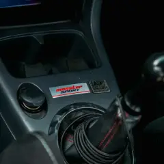 Wnętrze samochodu z naklejką "Monster Sport" i gniazdem zapalniczki. Który bezpiecznik jest od zapalniczki?