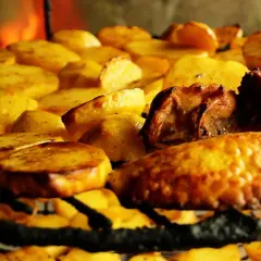 Patatas asadas y carne sobre una parrilla, un delicioso plato de comida típica de Armenia, con fuego al fondo.