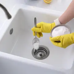 Main jaune versant du percarbonate dans un évier blanc pour le déboucher. Solution écologique et efficace.