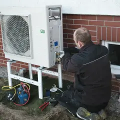 Instalator pracuje nad pompą ciepła, zapewniając jej ekonomiczne ustawienie. Widać narzędzia i sprzęt do montażu.