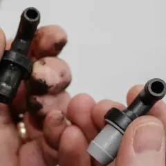 Manos sostienen dos válvulas PCV, una vieja y sucia, la otra nueva y gris.