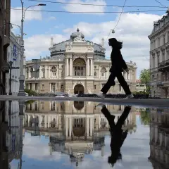 Kobieta idzie przez kałużę przed Teatrem Opery i Baletu w Odessie, tworząc odbicie niczym z filmu.