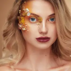Fotografia beauty: blondynka z niebieskimi oczami, makijażem inspirowanym naturą i ozdobami z suszonych kwiatów na twarzy.