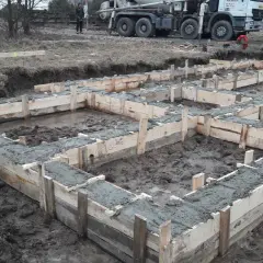 Rozpoczęła się budowa domu drewnianego. Wylano fundamenty, widać drewniane szalunki i świeży beton. W tle stoi gruszka z betonem.