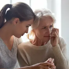 Młoda kobieta pociesza płaczącą starszą panią, która ociera łzy. Rozmowa o tym, co po śmierci, jest trudna, ale wsparcie jest ważne.