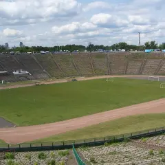 Stadion z PRL z murawą, bramkami i trybunami, w tle panorama Warszawy.