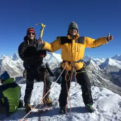 Dwóch alpinistów na szczycie Mera Peak, jeden z czekanem, drugi z kciukiem w górę. W tle ośnieżone góry.