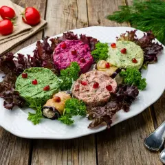 Talerz z gruzińskimi pastami pkhali: zielone, różowe i beżowe, ozdobione granatem i ziołami.