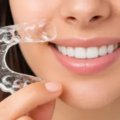 Una mujer muestra su sonrisa perfecta con un alineador transparente Invisalign.