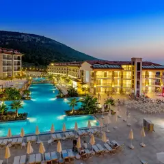 Piękny kompleks basenów i budynków hotelowych oświetlony wieczorem. Wiele osób szuka ramada resort akbuk opinie, by zaplanować wakacje.