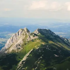 Górskie szczyty z zielonymi zboczami i kamienistymi graniami, w oddali widać dolinę i chmury.